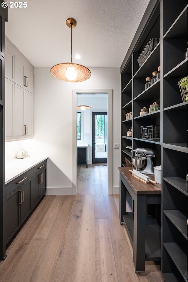 interior space with light wood-style flooring, baseboards, pendant lighting, and a textured ceiling