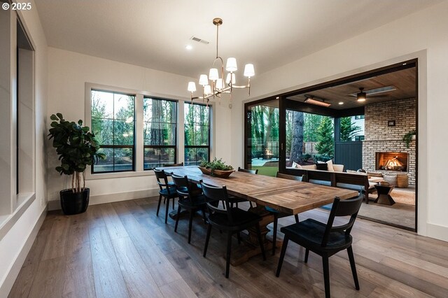 dining room with ceiling fan with notable chandelier, visible vents, baseboards, a brick fireplace, and wood-type flooring