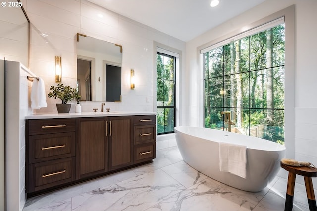 bathroom featuring marble finish floor, tile walls, recessed lighting, vanity, and a freestanding tub