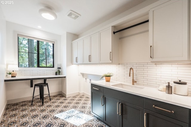 kitchen with a sink, visible vents, baseboards, light countertops, and decorative backsplash