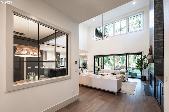 living area featuring baseboards, wood-type flooring, an inviting chandelier, a high ceiling, and recessed lighting