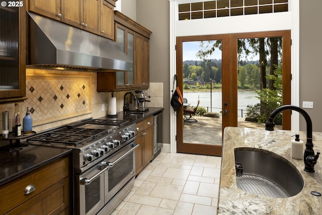 kitchen with a sink, decorative backsplash, under cabinet range hood, and double oven range
