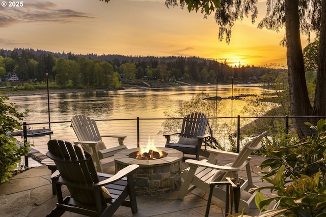view of patio / terrace with a water view, a fire pit, and a wooded view