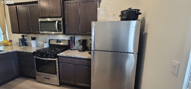 kitchen with appliances with stainless steel finishes, light stone countertops, dark brown cabinetry, and light wood finished floors