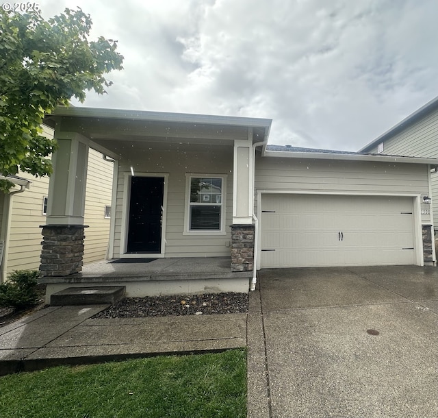 view of exterior entry featuring concrete driveway, a garage, stone siding, and a porch