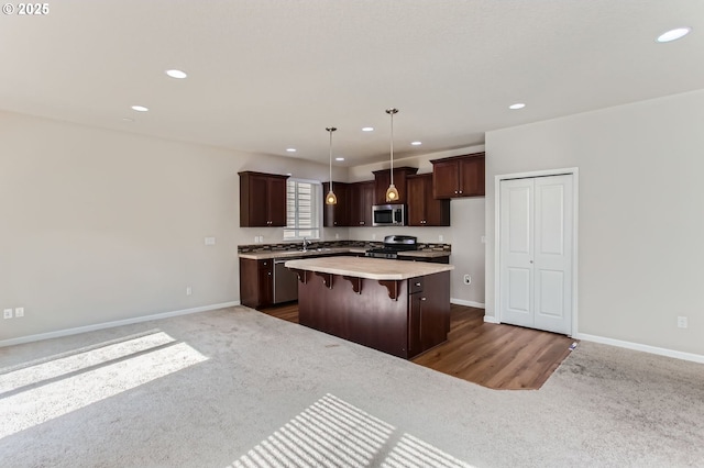 kitchen with a sink, stainless steel appliances, light countertops, dark colored carpet, and a center island