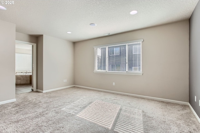 unfurnished room with visible vents, light colored carpet, a textured ceiling, and baseboards