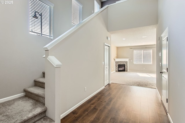 staircase featuring baseboards, a high ceiling, wood finished floors, and a tiled fireplace