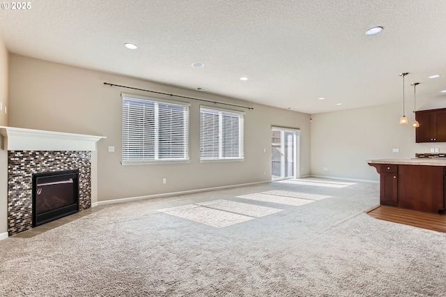 unfurnished living room with a tiled fireplace, light colored carpet, a textured ceiling, and baseboards