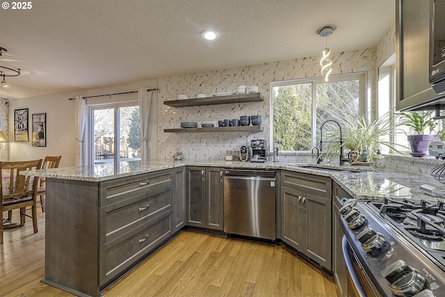 kitchen featuring light stone countertops, kitchen peninsula, stainless steel appliances, and hanging light fixtures