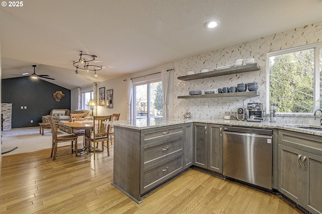 kitchen with light stone countertops, a textured ceiling, stainless steel dishwasher, kitchen peninsula, and vaulted ceiling