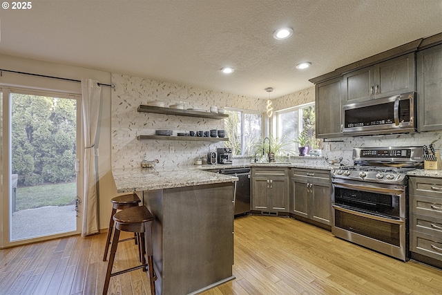 kitchen featuring light hardwood / wood-style floors, hanging light fixtures, a kitchen breakfast bar, sink, and stainless steel appliances