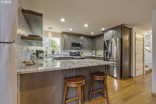 kitchen featuring kitchen peninsula, tasteful backsplash, light stone countertops, light hardwood / wood-style floors, and stainless steel appliances