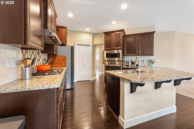 17202 NW Viola St, Portland, OR 97229 - kitchen with under cabinet range hood, a sink, stainless steel appliances, a breakfast bar, and backsplash