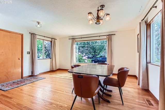 dining room with light wood-type flooring, baseboards, a chandelier, and a textured ceiling