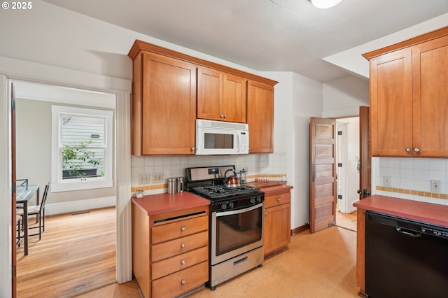 kitchen featuring white microwave, stainless steel gas stove, dishwasher, decorative backsplash, and brown cabinetry