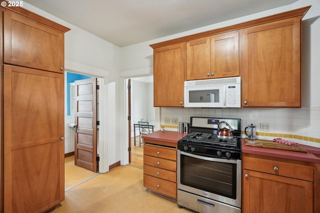 kitchen featuring white microwave, stainless steel range with gas cooktop, brown cabinets, and decorative backsplash