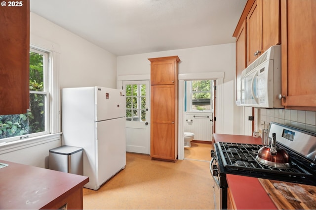 kitchen with white appliances, plenty of natural light, backsplash, and brown cabinets