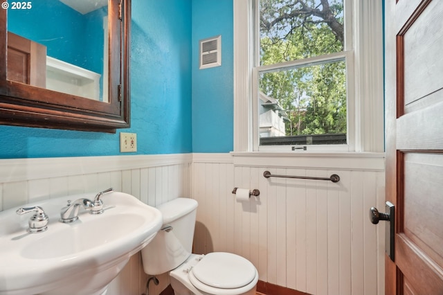 half bathroom featuring a sink, wainscoting, and toilet