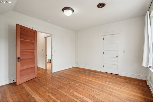 empty room featuring light wood-style floors, baseboards, and vaulted ceiling