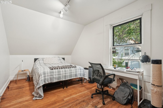 bedroom with wood finished floors, vaulted ceiling, track lighting, and baseboards