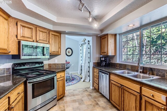 kitchen featuring brown cabinets, a tray ceiling, stainless steel appliances, a textured ceiling, and a sink