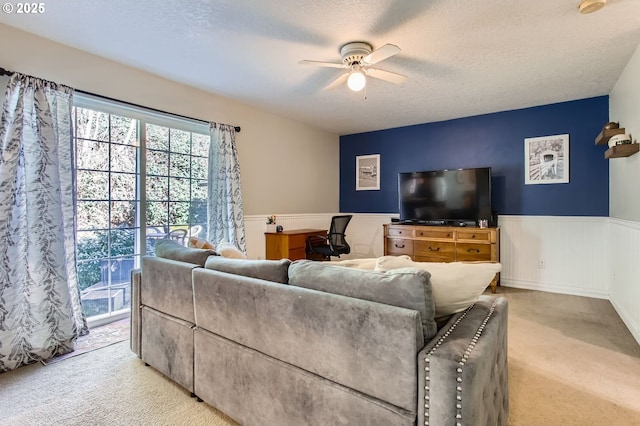 living room featuring wainscoting, ceiling fan, light carpet, and a textured ceiling