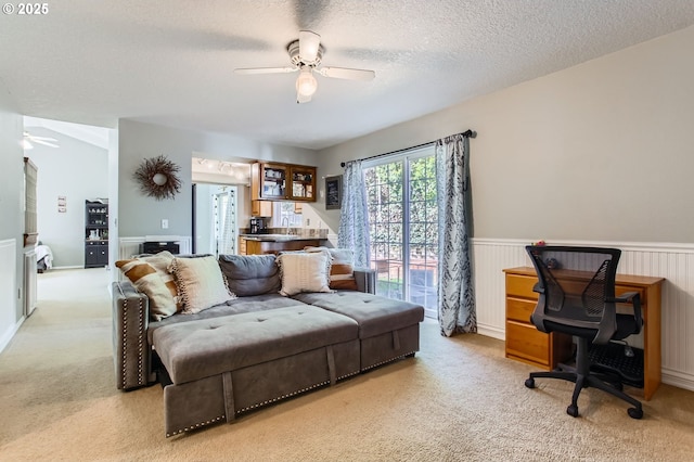 interior space featuring wainscoting, ceiling fan, light carpet, and a textured ceiling