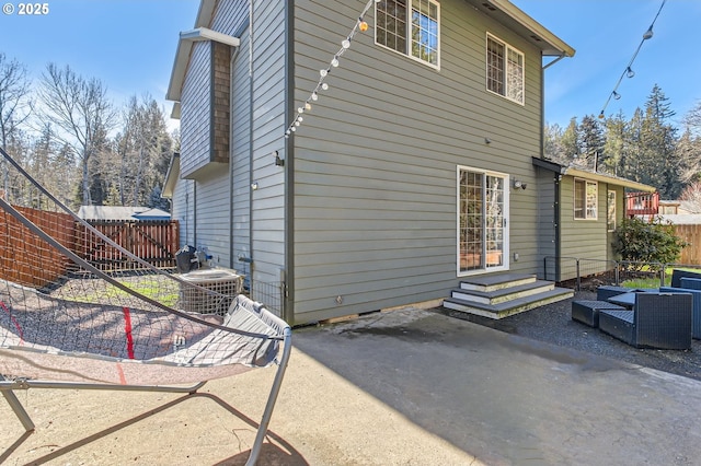 rear view of house with entry steps, central air condition unit, fence, and a patio