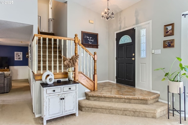 carpeted foyer featuring a notable chandelier, stairway, and baseboards