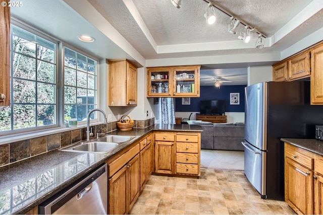 kitchen featuring a textured ceiling, appliances with stainless steel finishes, brown cabinetry, and a sink