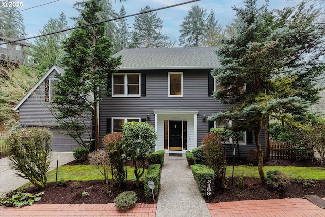 colonial home featuring a shingled roof, concrete driveway, an attached garage, and fence