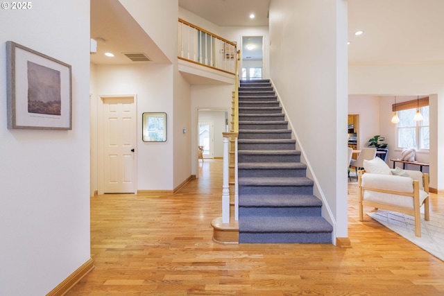 staircase featuring wood finished floors, visible vents, a towering ceiling, and baseboards