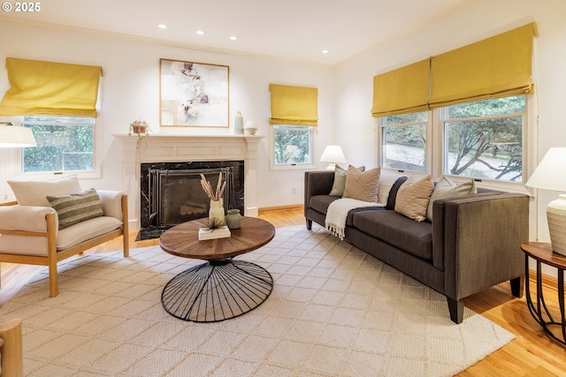 living area featuring a high end fireplace, baseboards, light wood-style floors, and ornamental molding