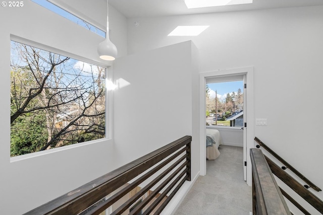 hall with light carpet, a skylight, a towering ceiling, and an upstairs landing