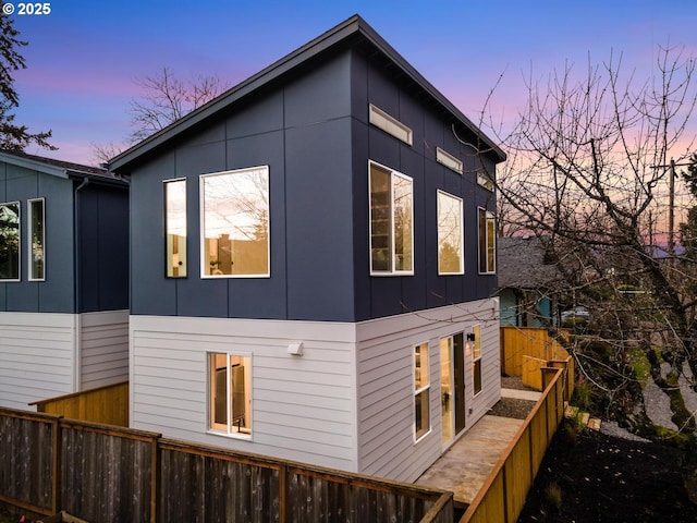 property exterior at dusk featuring fence and board and batten siding