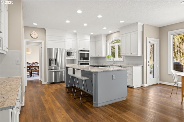 4679 Dogwood Dr, Lake Oswego, OR 97035 - kitchen featuring appliances with stainless steel finishes, a center island, dark wood-style floors, white cabinetry, and a kitchen breakfast bar