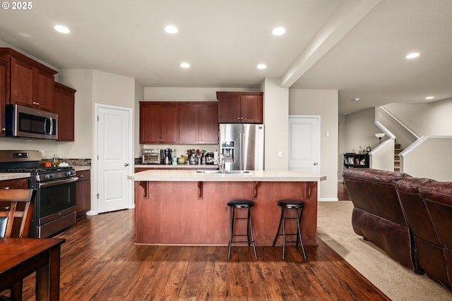 kitchen with appliances with stainless steel finishes, a sink, light countertops, open floor plan, and dark wood-style floors