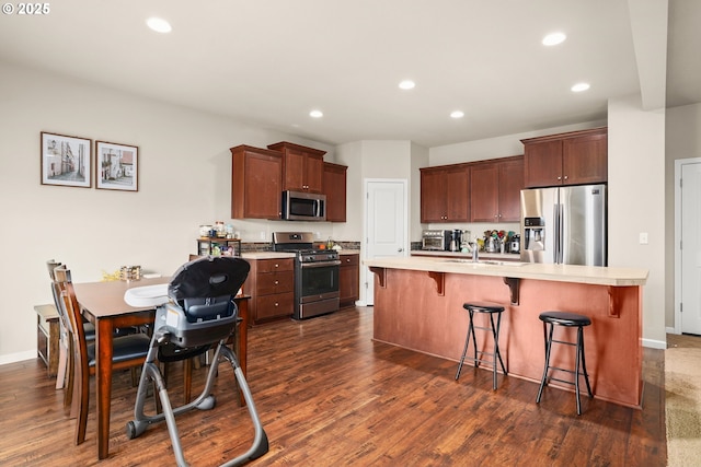 kitchen featuring a kitchen bar, light countertops, dark wood-style floors, stainless steel appliances, and recessed lighting