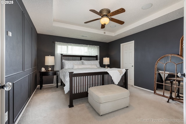 bedroom featuring light carpet, ceiling fan, a tray ceiling, and a textured ceiling