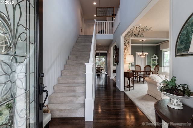 entrance foyer featuring crown molding, dark wood-type flooring, an inviting chandelier, and a towering ceiling