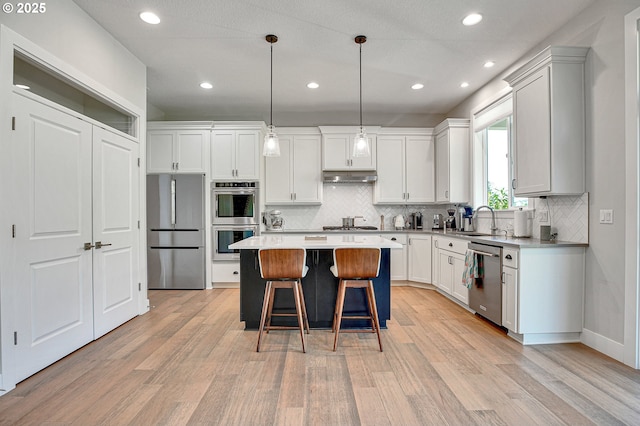 kitchen featuring a sink, light wood-style flooring, under cabinet range hood, and stainless steel appliances