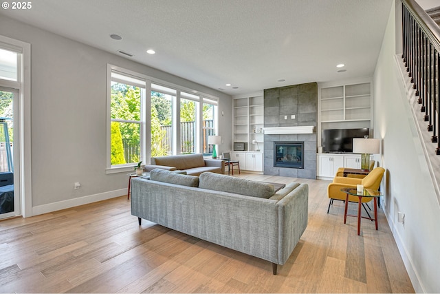 living room featuring baseboards, a tiled fireplace, a wealth of natural light, and light wood finished floors