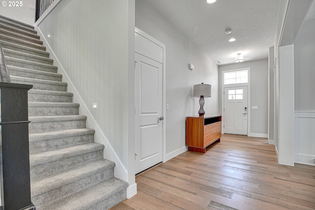 foyer entrance with baseboards, a textured ceiling, wood finished floors, and stairway