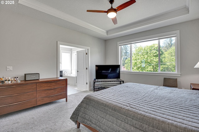 bedroom with crown molding, connected bathroom, light colored carpet, a textured ceiling, and a tray ceiling