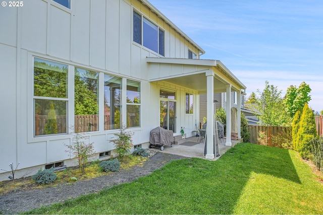 rear view of property featuring board and batten siding, a lawn, fence, and a patio area
