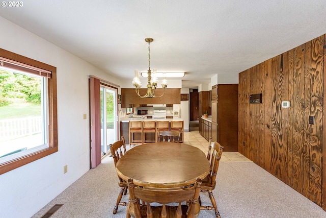 carpeted dining area with wooden walls and an inviting chandelier