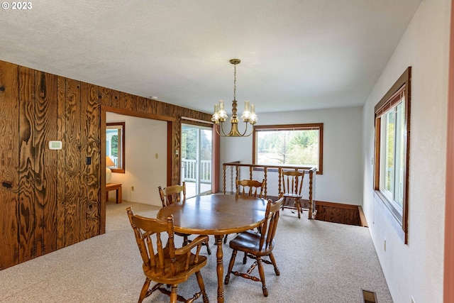 dining space featuring a notable chandelier, light colored carpet, a textured ceiling, and wooden walls