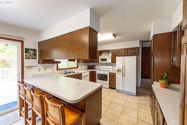 kitchen featuring white appliances, a kitchen breakfast bar, sink, light tile patterned floors, and kitchen peninsula