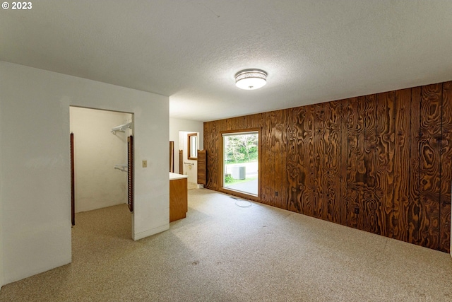 carpeted spare room with a textured ceiling and wood walls